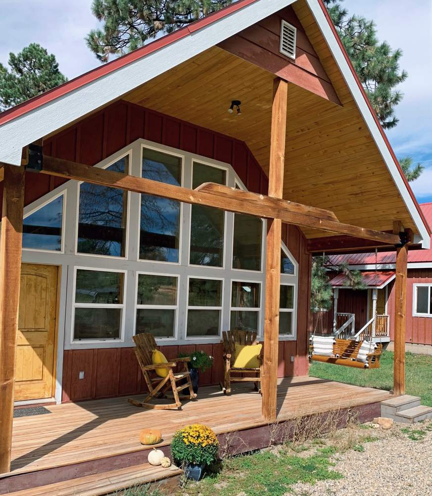 The A-frame cabin's tall window wall and timber porch with deck chairs