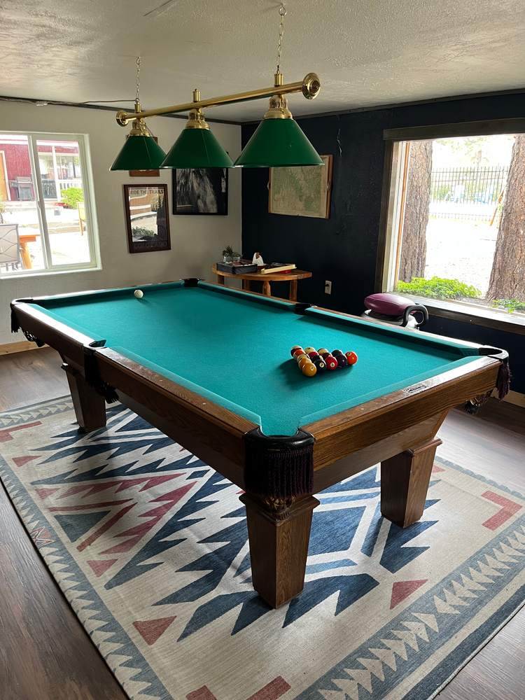 Pool table under green billiard lamps in the ranch game room